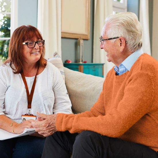 a support worker is assisting an elderly gentleman. They are seated on a couch discussing something.